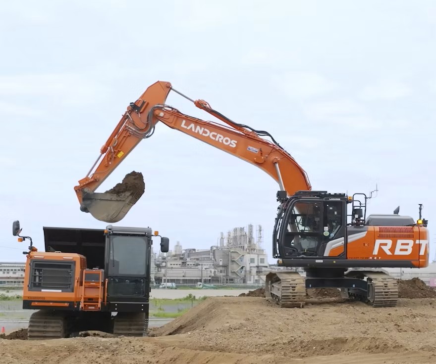 Landcros excavator (Hitachi Construction Machinery) loading a dump truck on a construction site in Japan, 2026